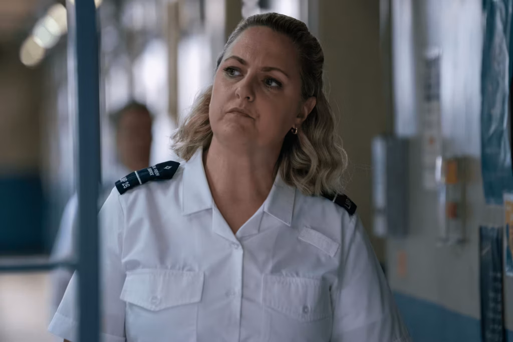 Woman in a prison officer outfit standing in a cell block.