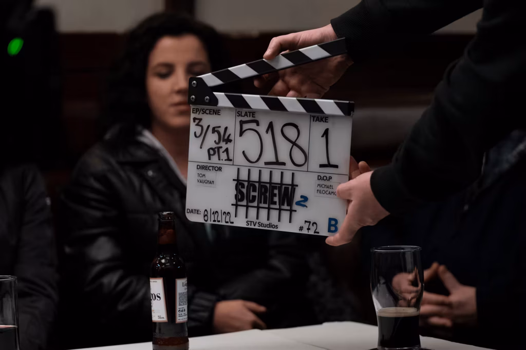 Woman sitting behind a film slate (clapperboard) marked with a scene number during filming.