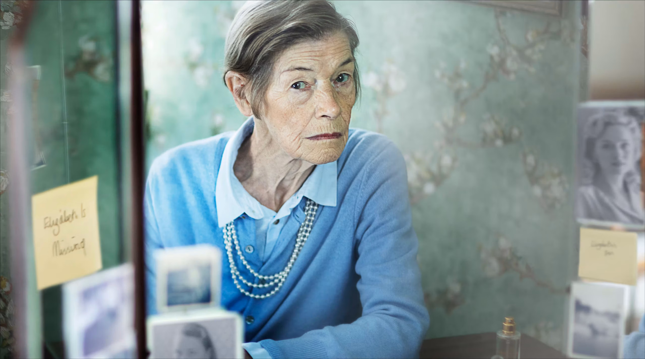 Elderly woman sitting at a vanity table.