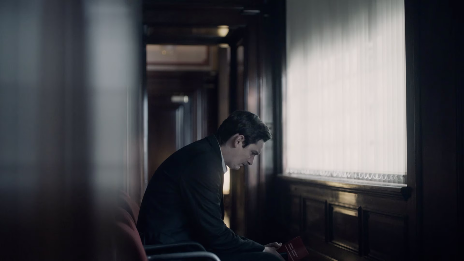 Man in a courtroom hallway looking down with a worried expression.