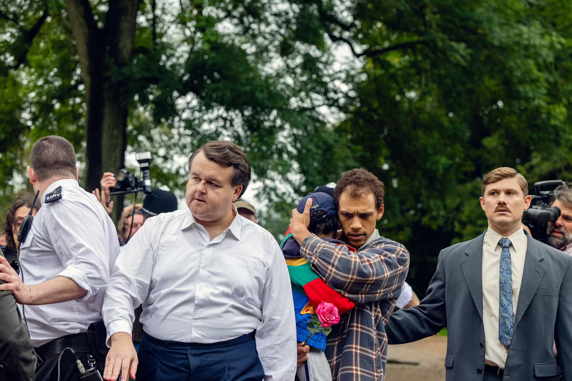 A man holding his child in his arms while officers and press photographers take pictures around them.