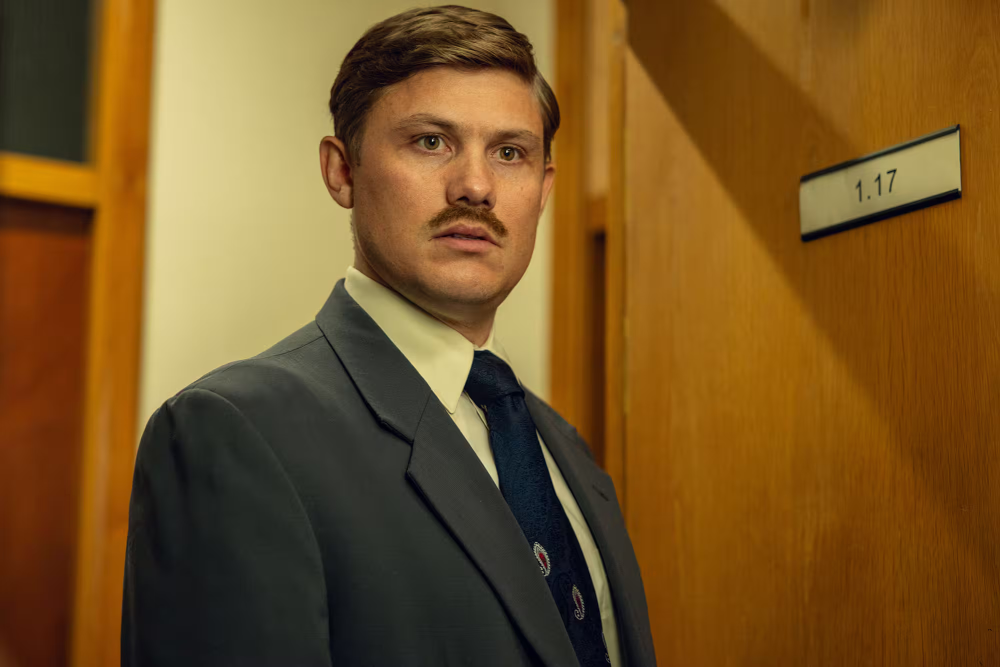 A man stands in a doorway with a serious expression.