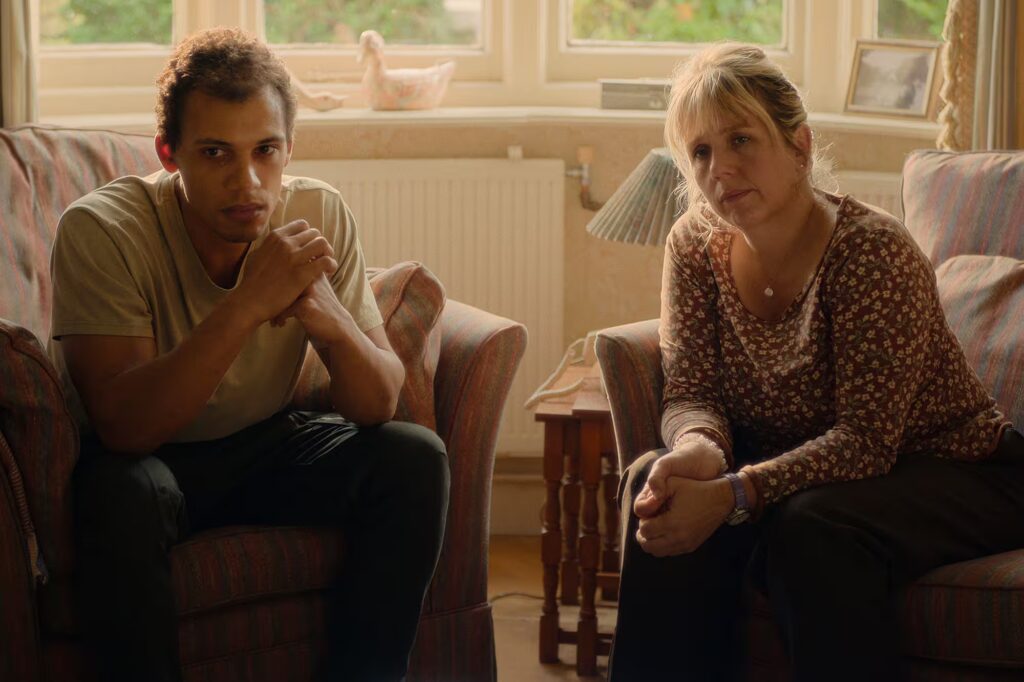 Man and woman sitting in a living room setting, looking forward with concerned expressions.